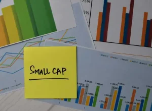 Post it note with "Small Cap" written on it amid a background of charts.